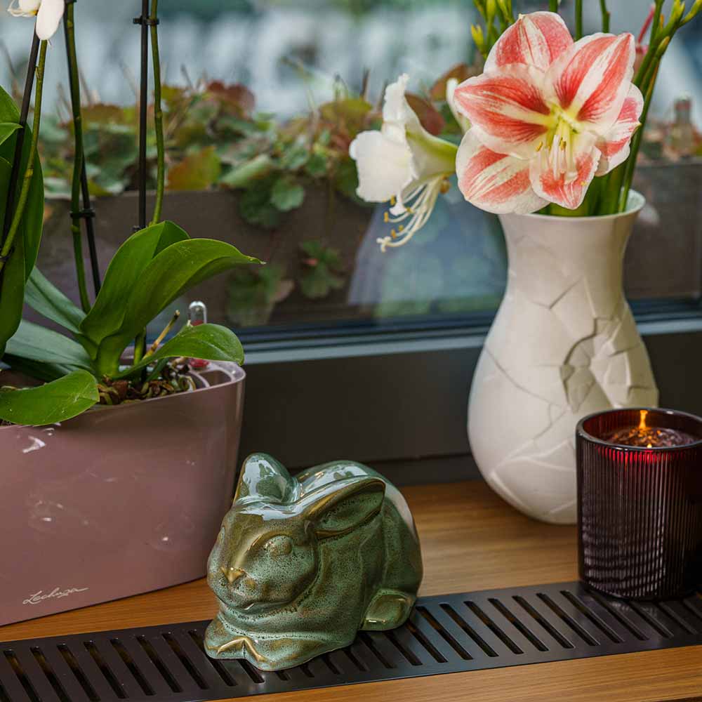 Rabbit Urn For Ashes Oily Green By Window Facing Front Left With Flowers Close Up